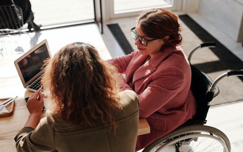 two women working on laptop, one in a wheelchair